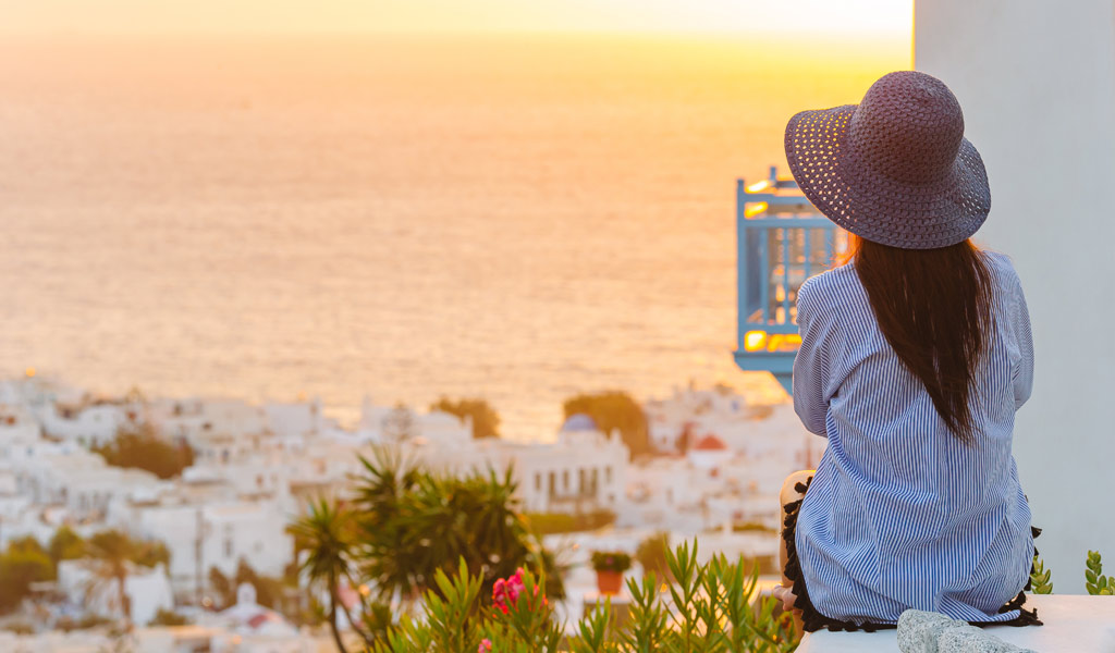 Young Woman is Looking at the Sunset Over A Sea In Famous Mykonos Greece